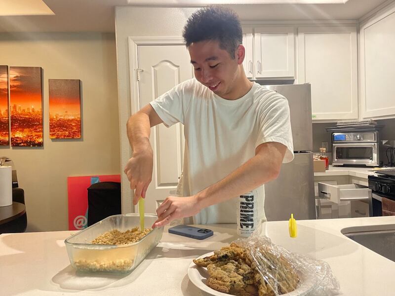 Huey wears a white t-shirt while cutting rice krispies treats and has an open plate of cookies in front of him.