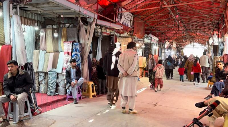 Outdoor market where vendors are standing next to their outdoor markets. Fabrics is hung up in each section.