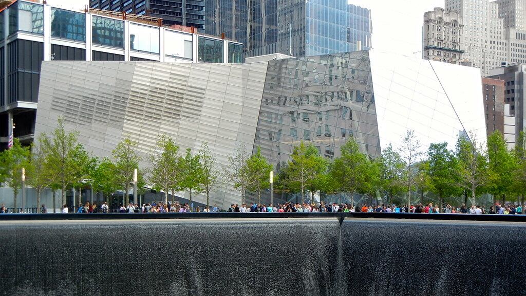 A water flows into a pool with buildings and a crowd of people behind it in New York City.