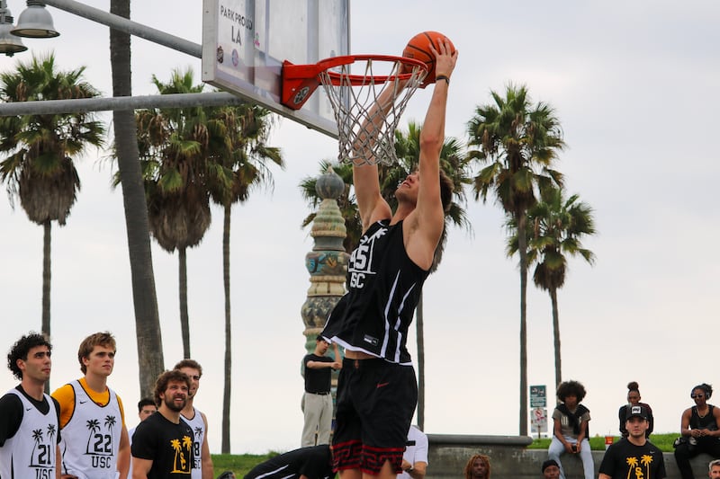 Gabe Dynes (45) rises up to dunk a basketball in a net. He wears a black USC basketball jersey with white accents.