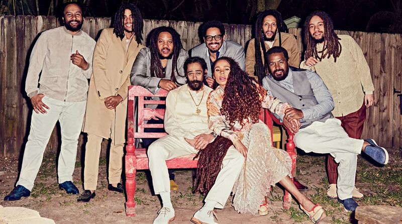 Nine of Marley's children pose together while wearing beige, white and gray. Three sit on a bench and the rest stand behind.