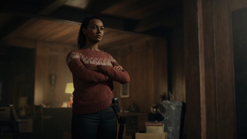 Video game screenshot of a woman wearing a sweater in a cabin
