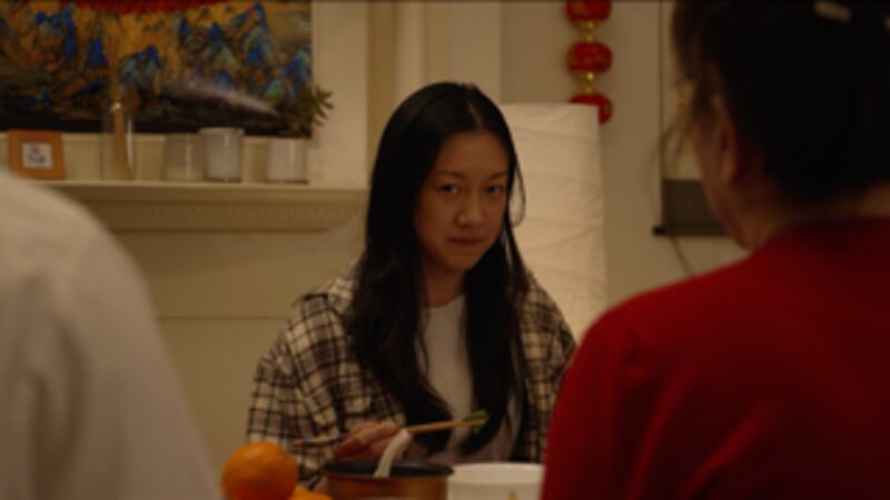Film still of a woman sitting at a dinner table