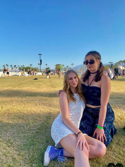 A photo of Murphy and another woman posing and smiling for the camera. They are sitting on grass and the festival grounds are in the background.