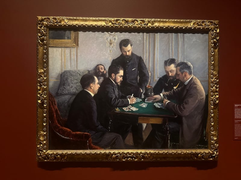 The painting is against a dark red wall and placed in a gold frame.