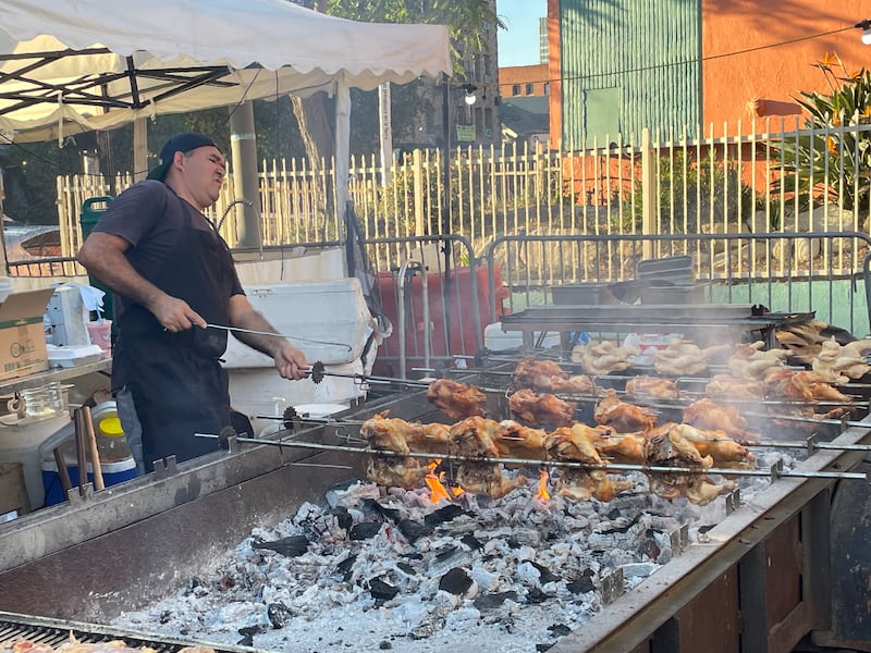Photo of a man turning several large skewers with four whole chickens on it over an open flame