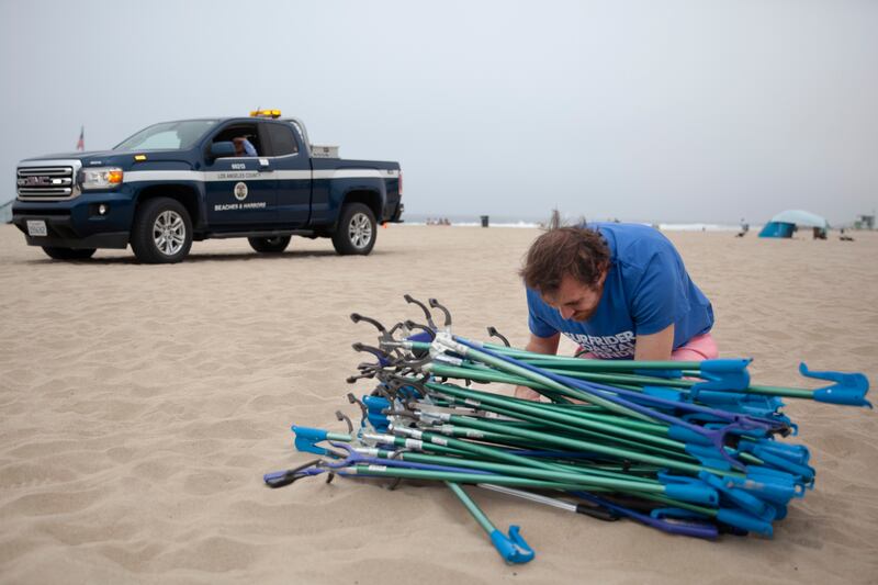 A volunteer at Venice Beach putting down a pile of trash pickup sticks.
