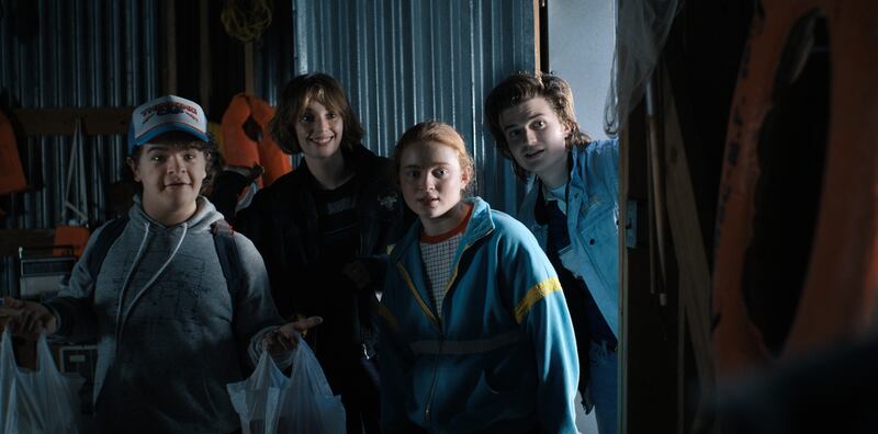 A photo of four actors from Stranger Things in a dark room looking at something off camera.