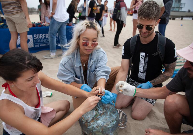 Volunteers at a beach cleanup filling up an empty water container with cigarette butts.