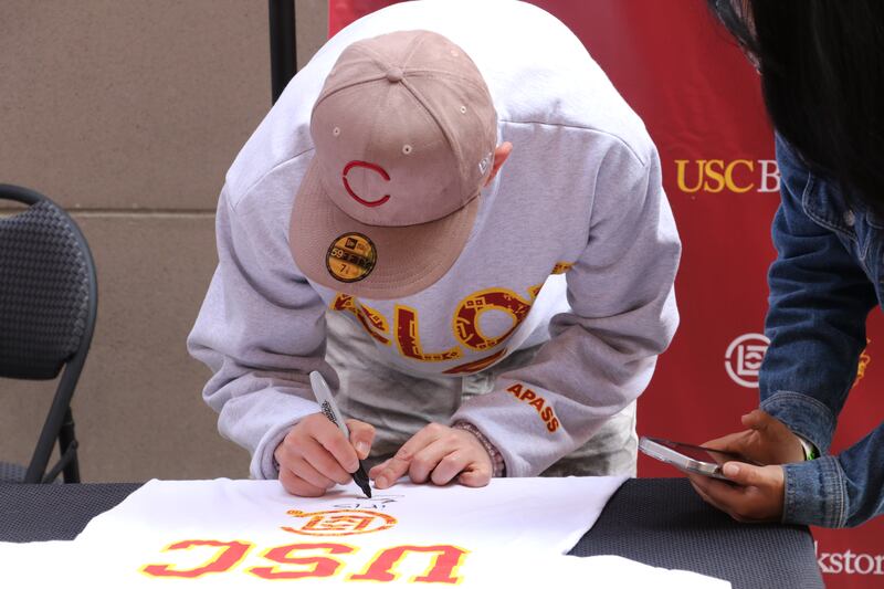 Photo of a man with a hat signing a t-shirt with a sharpie