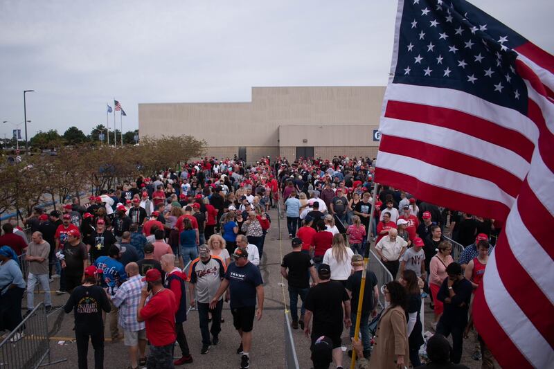 A line of people snaking around partitions, with an American flag in the foreground.