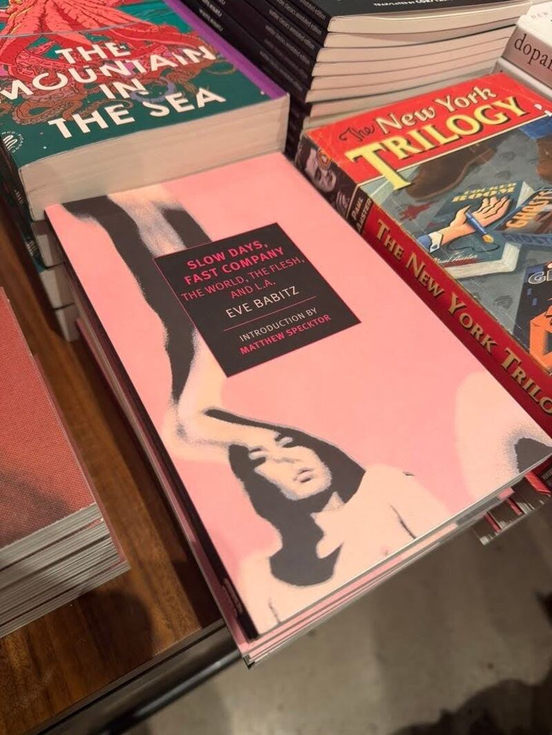 "Slow Days, Fast Company: The World, The Flesh, and L.A" by Eve Babitz takes place in 1970s California. Pink book cover with the photo of a woman