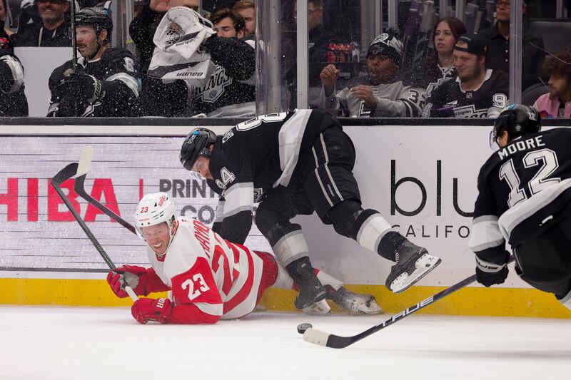 Detroit Red Wings left wing Lucas Raymond, left, reacts after colliding with Los Angeles Kings defenseman Vladislav Gavrikov, center, as left wing Trevor Moore controls the puck during the third period of an NHL hockey game Saturday, Nov. 16, 2024, in Los Angeles. (AP Photo/Ryan Sun)