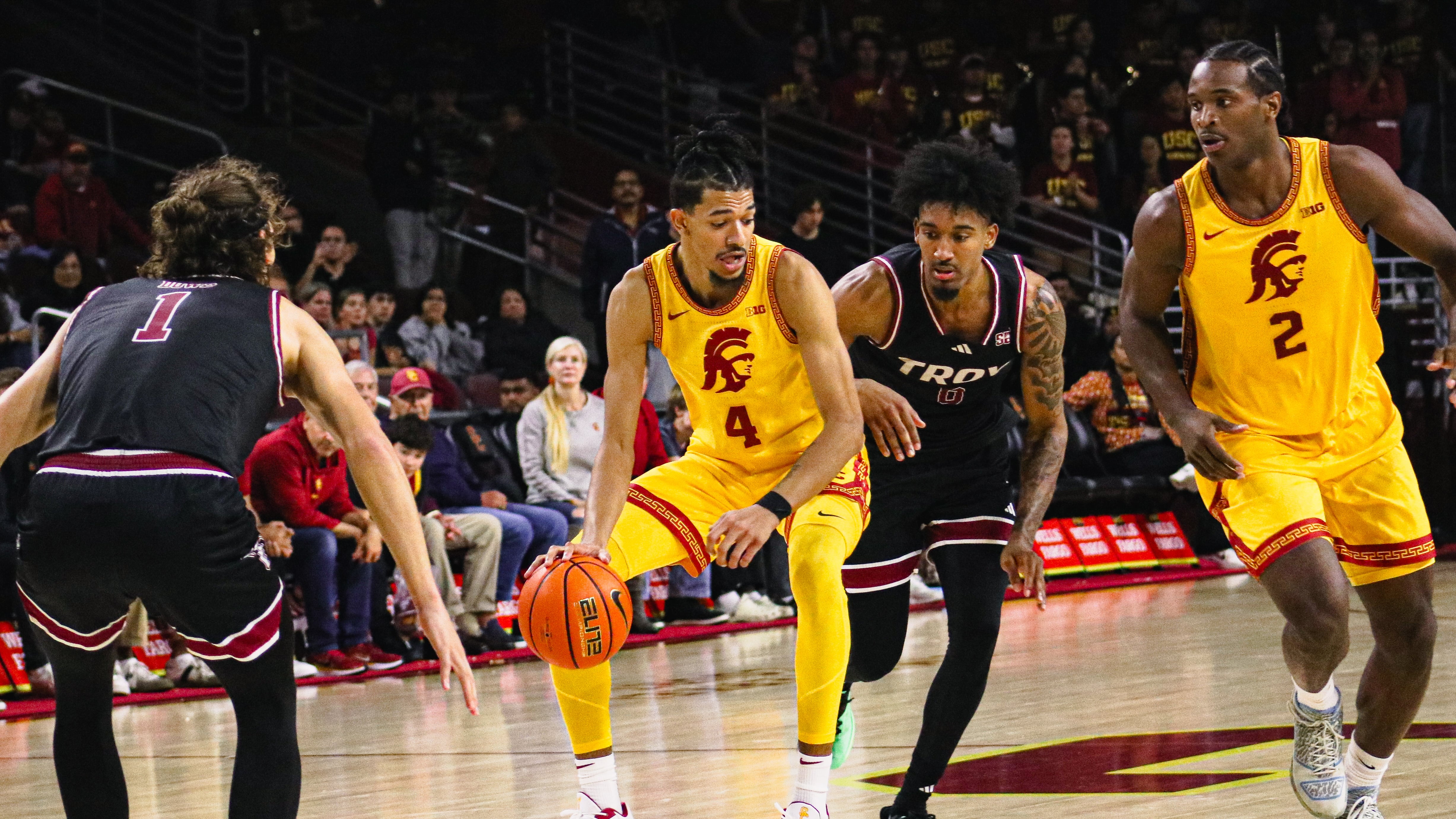 Chad Baker-Mazara dribbles the ball with one defender behind him and another in front, as Ezra Ausar trails closely behind.