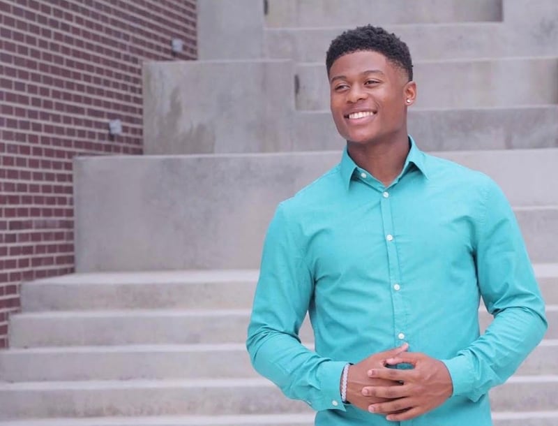 Jared Smith stands smiling on a set of concrete steps, wearing a teal button-down shirt and looking off to the side.