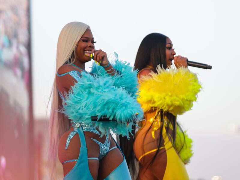 A photo of two women on stage singing into microphones. They are wearing blue and yellow feathery outfits.