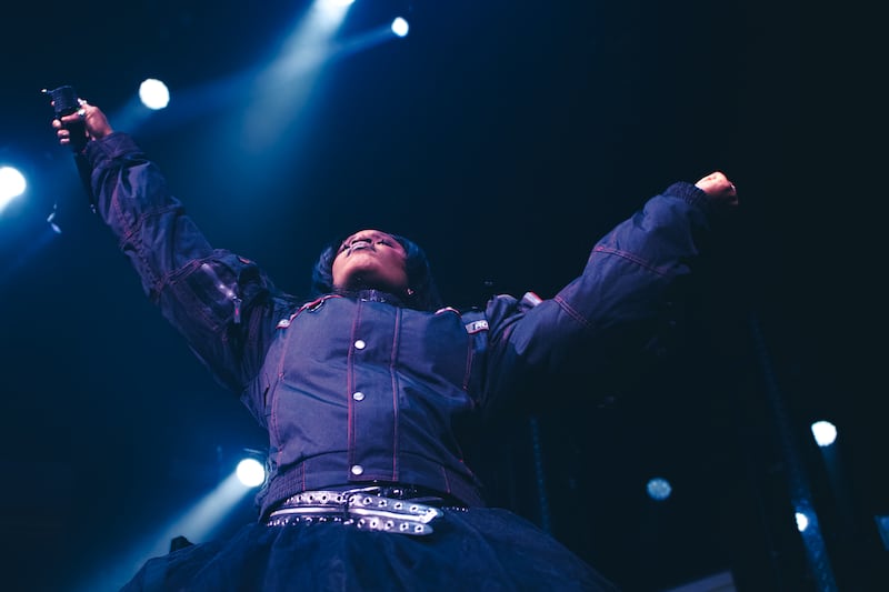 Photo of Amaarae with her hands in the air holding a microphone as she walks on the stage. Lights are shining on her.