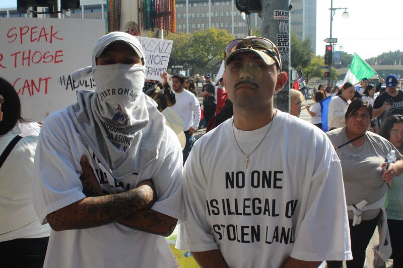 two men wearing 'no one is illegal on stolen land shirts'