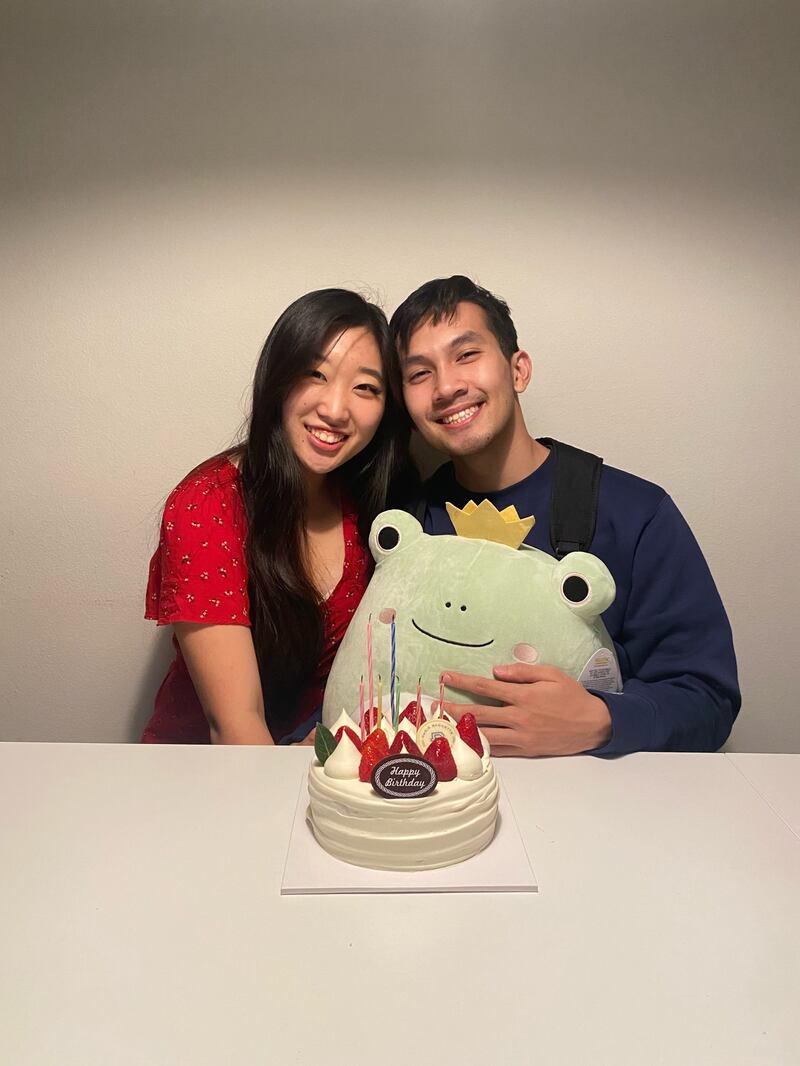 An Asian man and an Asian woman posing together in front of a cake. The man is holding a large frog plushie.