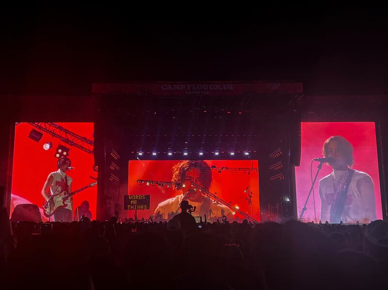 Photo of a large stage with three screens with a red background showing a man on them