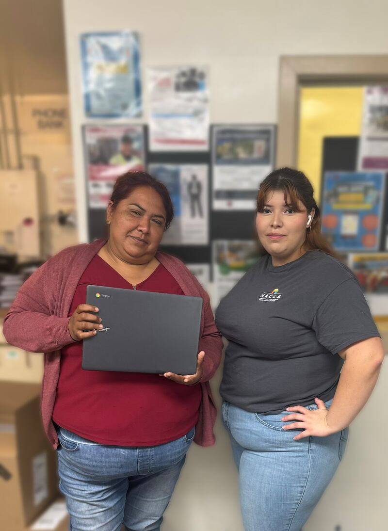 Photo of two women, the woman on the left is holding a laptop in her hands.