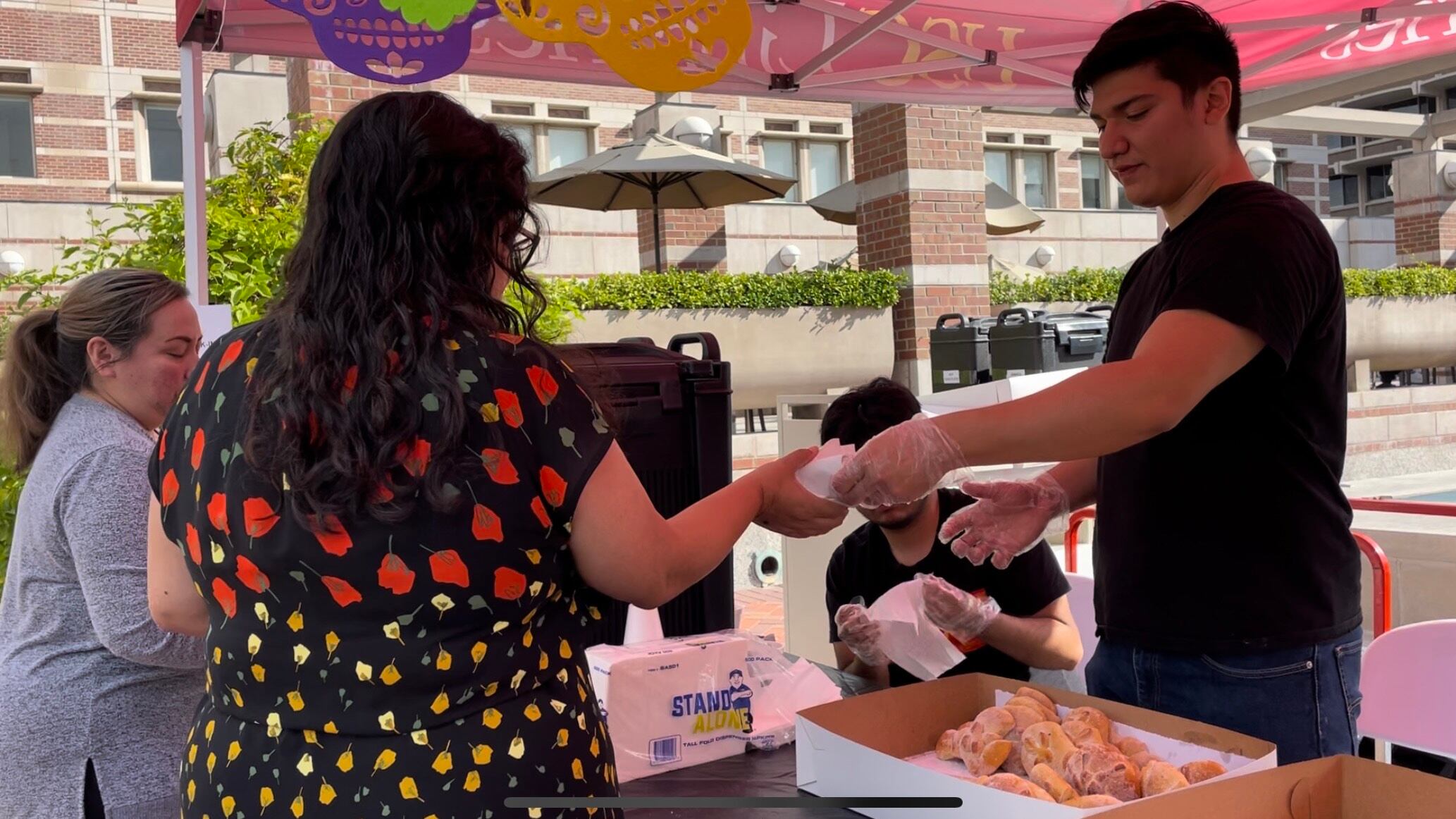 A volunteer is serving pan de muerto to a Dia de los Muertos celebration participant