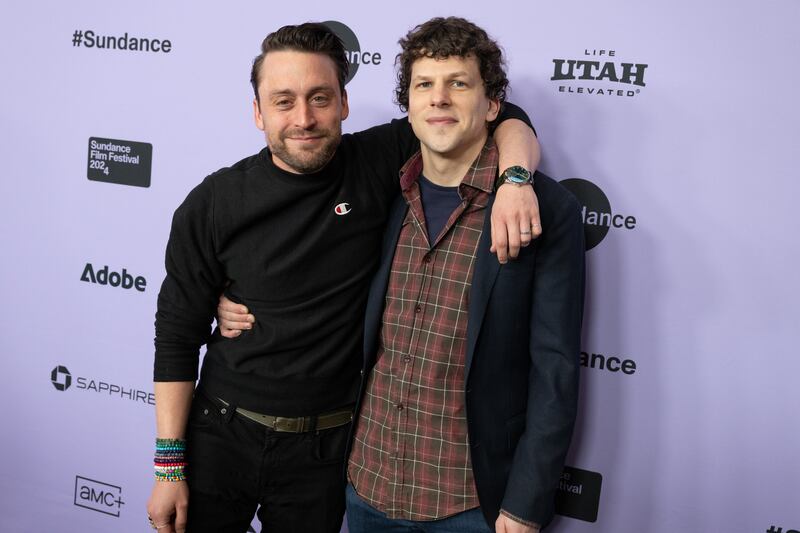 A photo of Kieran Culkin and Jesse Eisenberg posing next to each other and hugging while smiling at the camera on a red carpet at the Sundance Film Festival.