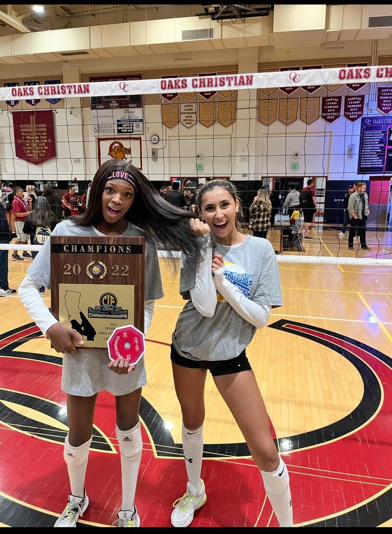 London Wijay and Alanah Clemente pose on Oaks Christian's volleyball court with the net behind them. Clemente holds a plaque that reads '2022 Ford Southern Section Champions'