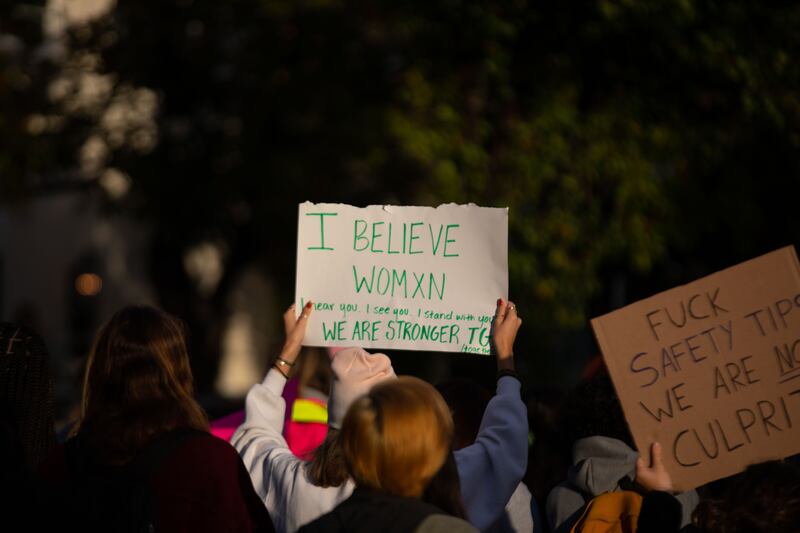 Students protest outside fraternities in October 2021, holding a sign that says "I belive womxn."
