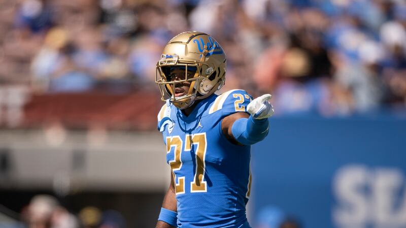 Kamari Ramsey, wearing a blue UCLA No. 27 jersey, points using his left hand.