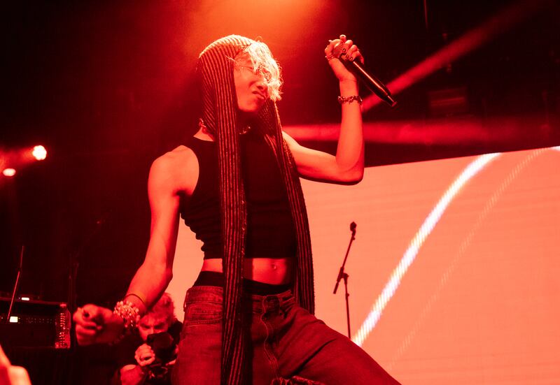 Photo of a man dancing on stage with a microphone wearing a hat that drapes down to his knees