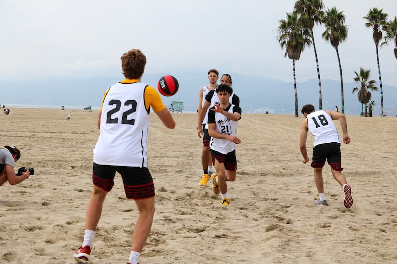 USC men's basketball players run through the sand passing a basketball back and forth.