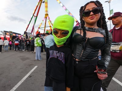 A photo of an alien prop wearing a green ski mask and Contarino with her arm around him wearing a black outfit.