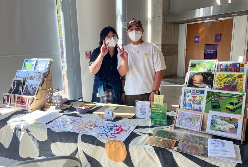 Photo of two people standing behind a booth with art on display