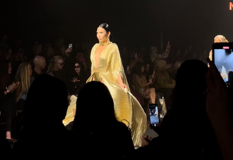 A model wears a shiny gold dress as the rest of the runway is black.