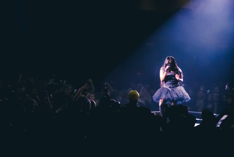 Photo of Amaarae singing at center stage. The spotlight only illuminates her, and the crowd is watching her.
