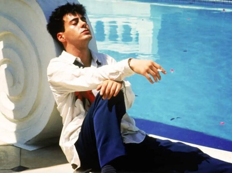 A man next to a pool smoking a cigarette with his head leaning back and his eyes closed.