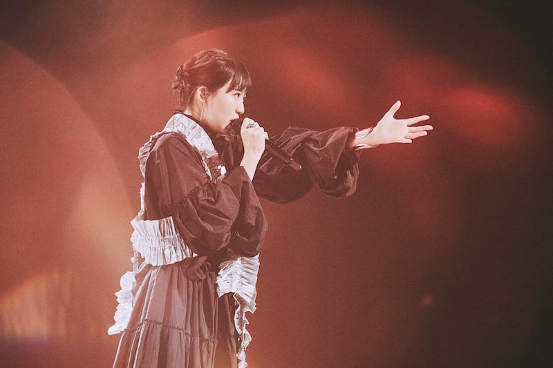 Japanese singer XAI extends her hand forward to the audience.