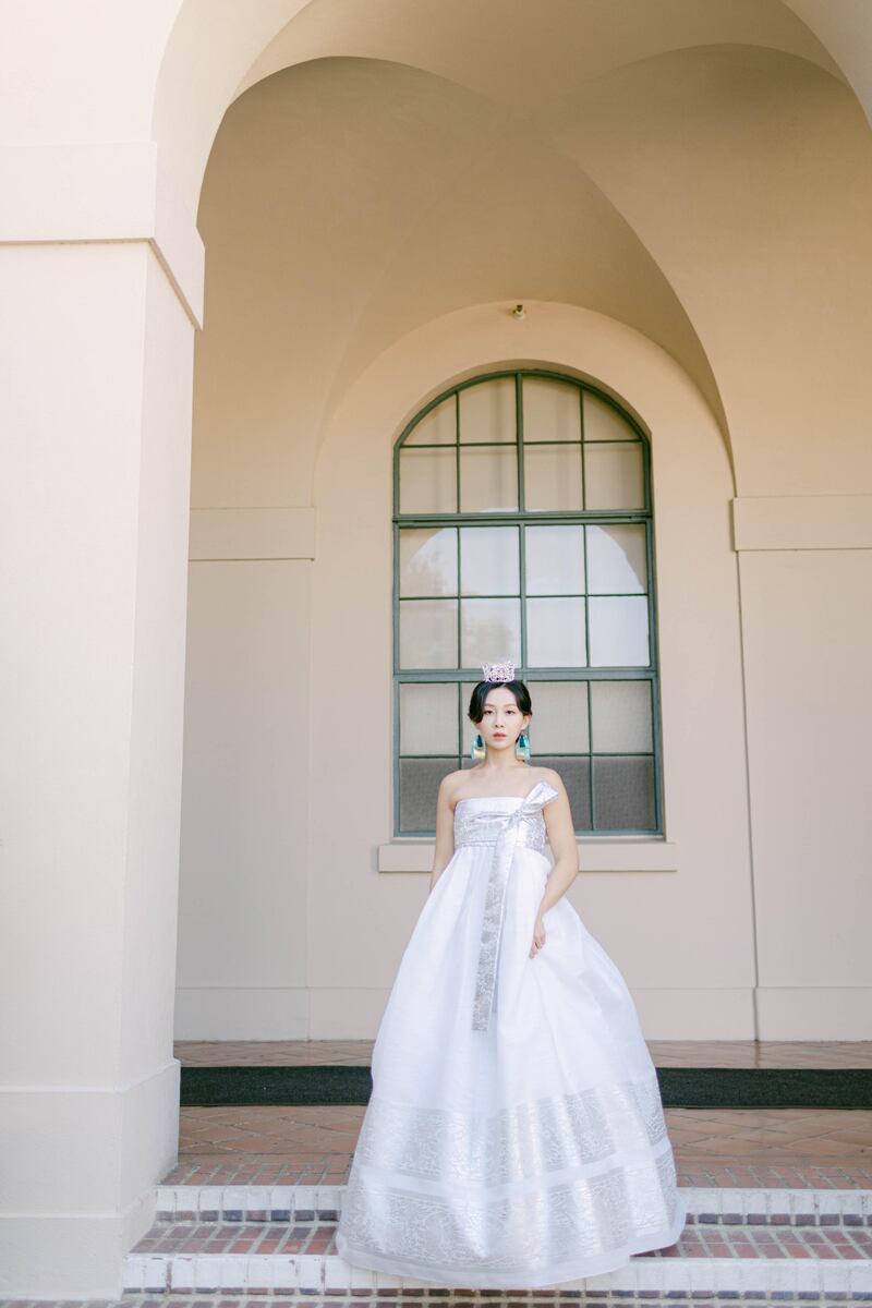 A photo of a woman wearing a white dress with a silk ribbon top half and a flow-y bottom half.