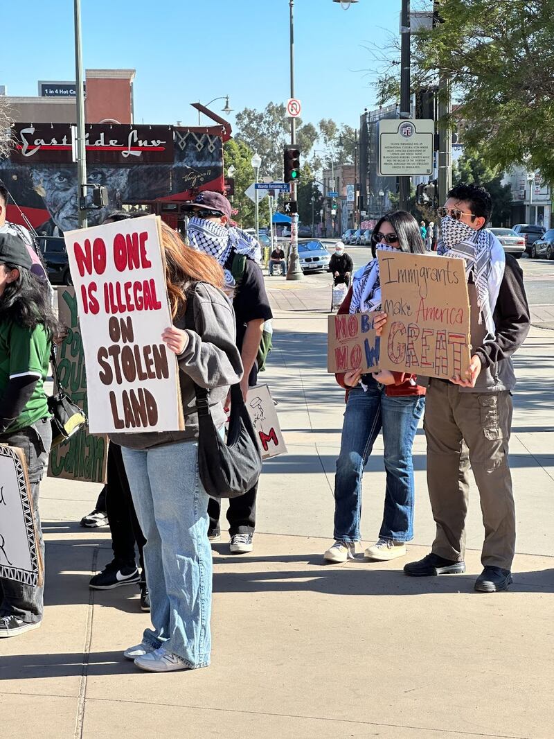 Photo of protestors outside holding signs. One reads 'No one is illegal on stolen land.'