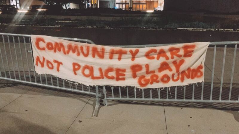 [Photo of banner reading "Community Care Not Police Playgrounds" in front of LAPD HQ.]