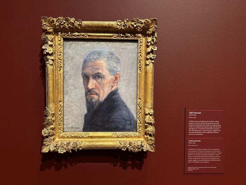 The painting is against a dark red wall and mounted in a gold frame.