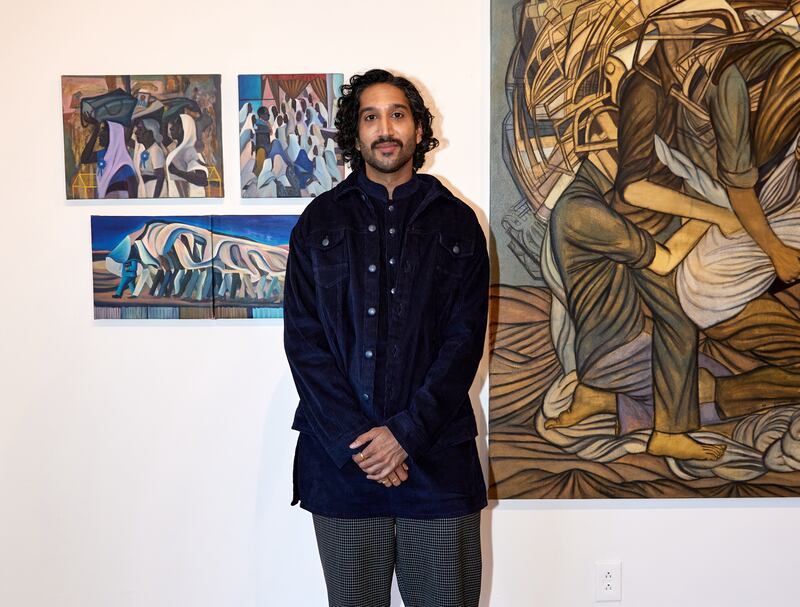 Photo of a man in a dark coat standing in front of paintings