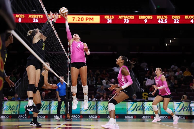 Reese Messer (3) jumps sideways and tips a volleyball over the net and the outstretched arms of an Oregon defender.