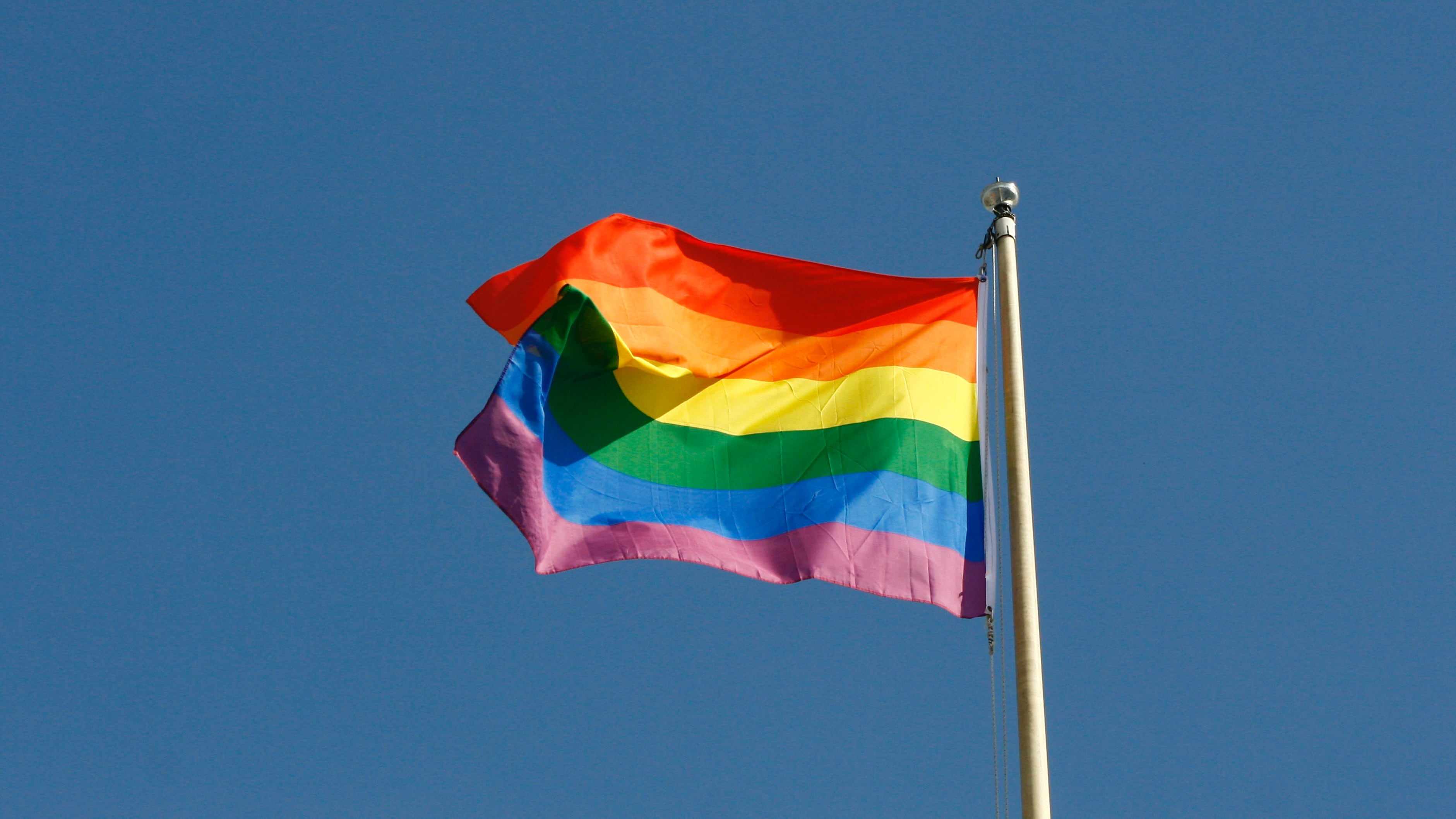 Photo of a rainbow flag on a pole with the sky in the background