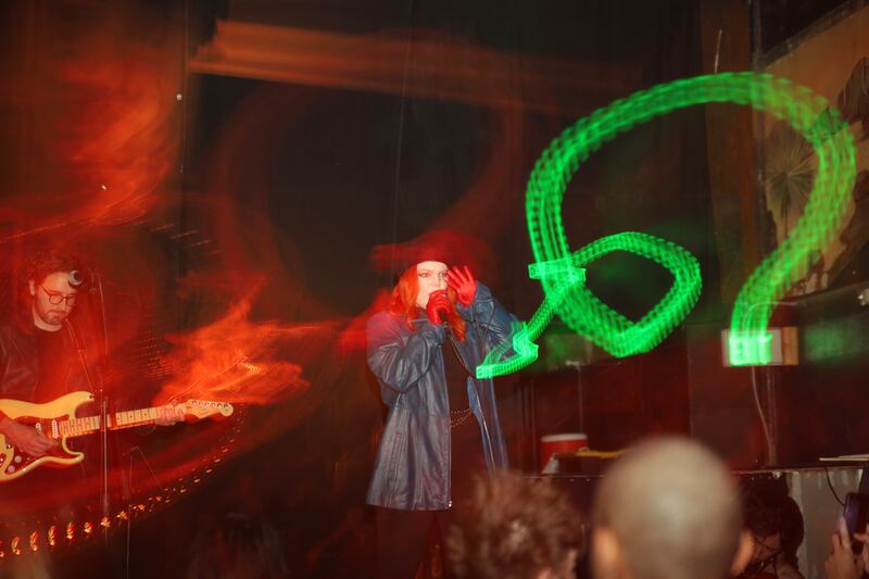 A photo of a musician performing onstage with neon lights around them.