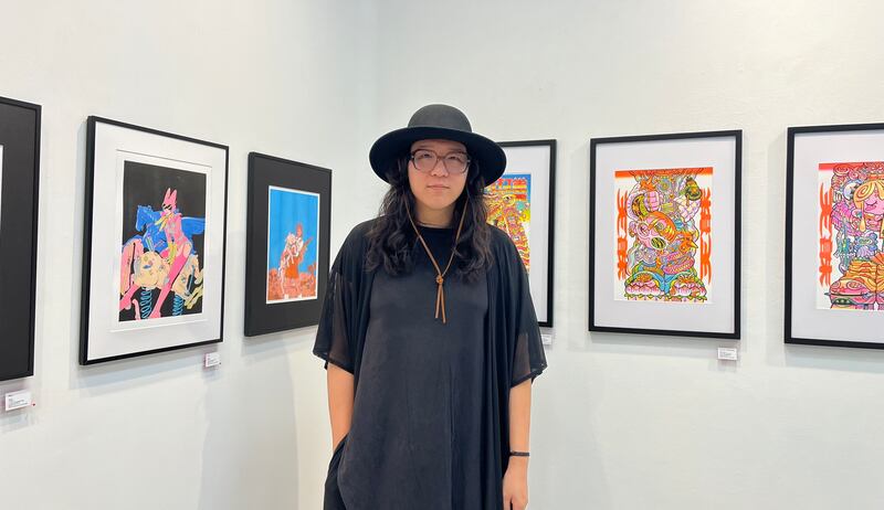 Photo of a person wearing a black shirt and large hat in front of framed artwork.