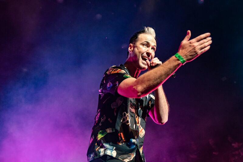 A photo of Fitzgerald passionately yelling into a microphone to the audience. There is a purple haze behind him in the background.