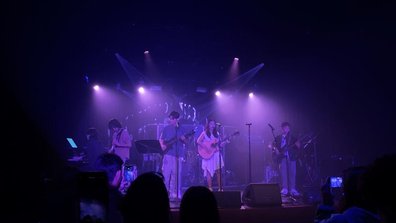 Photo of a band performing on a stage under purple light