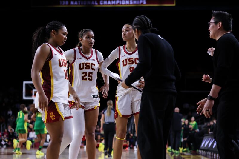 Malia Samuels (10), Kara Dunn (25) and Jazzy Davidson (9) huddle on the sideline with USC assistant coach Courtney Jaco, who holds a clipboard in her hand.